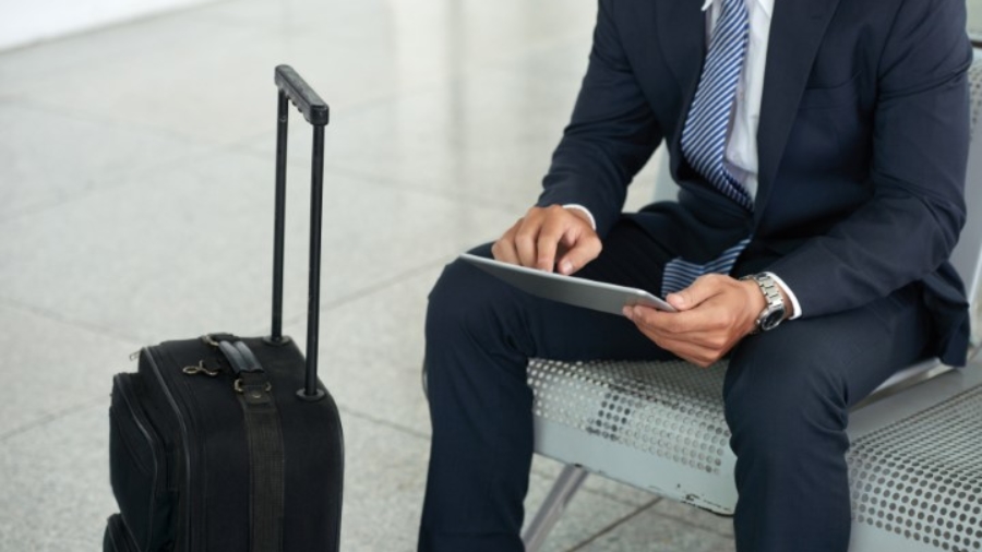 Mid section portrait of unrecognizable businessman using digital tablet while waiting in airport with suitcase